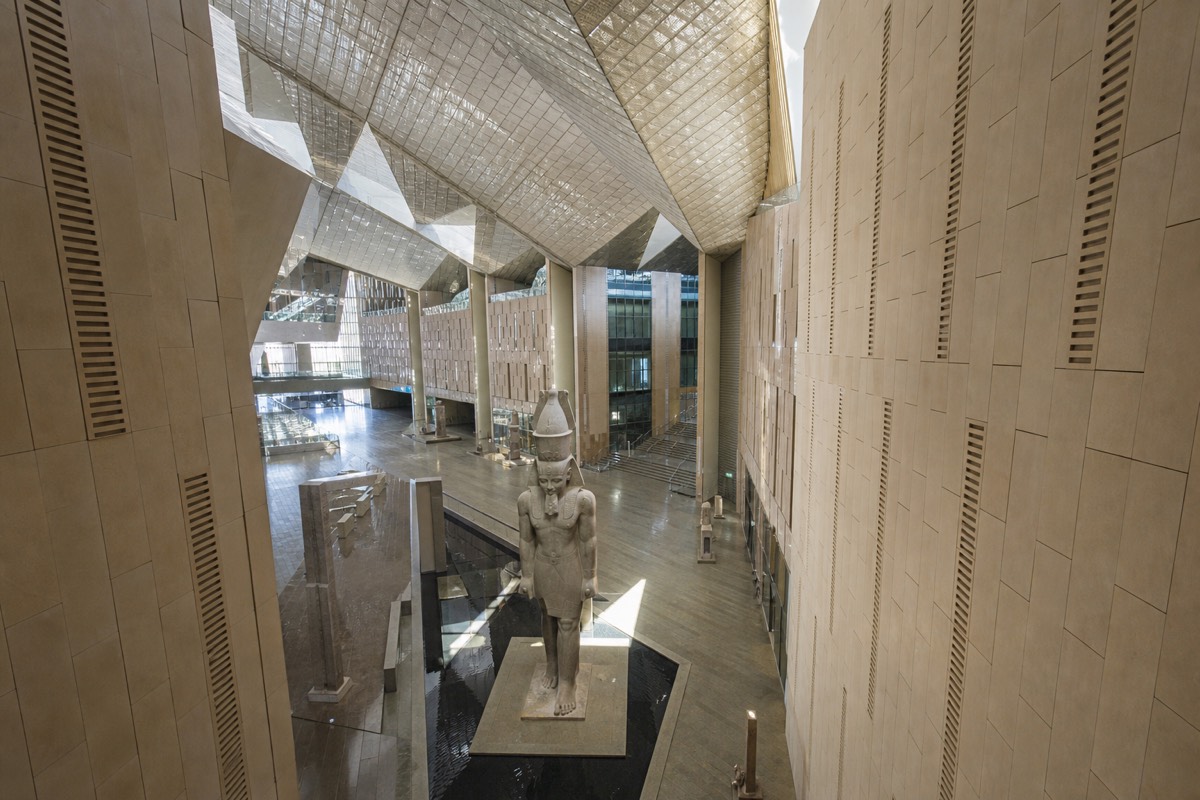 The soaring interior atrium of the Grand Egyptian Museum lit by daylight through the glass facade